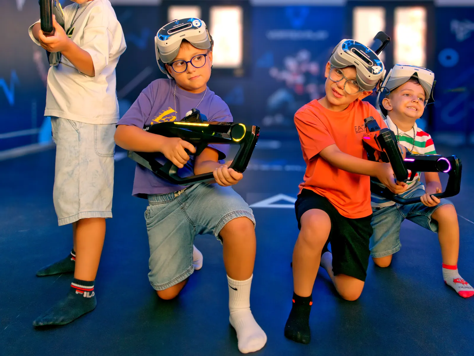 Four children in a VR arena, crouched in battle pose with headsets and Striker guns.